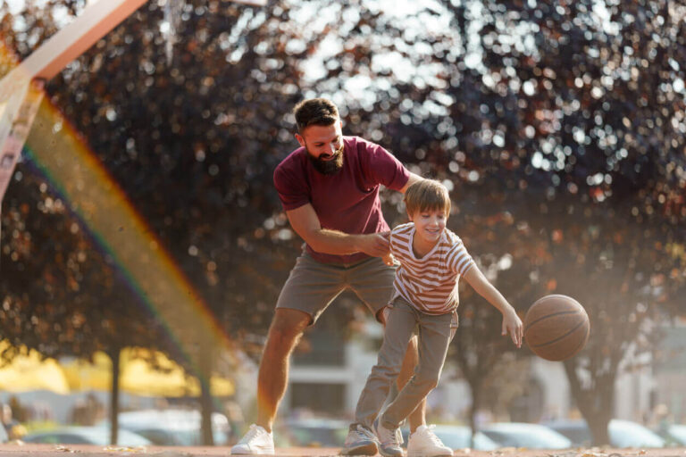 Pai e filho jogando basquete ao ar livre, demonstrando foco, coordenação e momentos de conexão que estimulam o desenvolvimento da TDAH e concentração por meio da prática de atividades físicas.