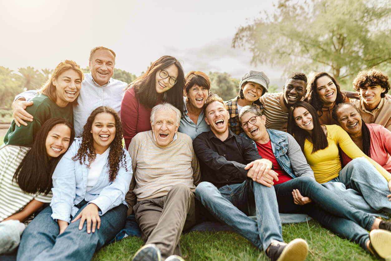 Grupo diverso de pessoas de várias idades sorrindo juntas ao ar livre, representando diferentes gerações e suas experiências com a saúde mental.