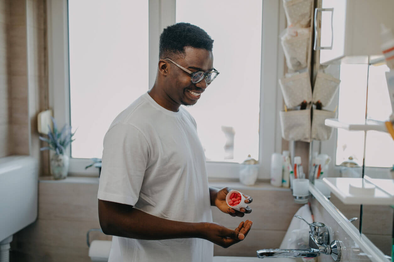 Homem sorrindo enquanto segura um pote de suplementos para imunidade, preparando-se para tomar as cápsulas.