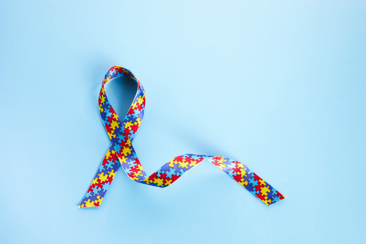 Fita colorida com peças de quebra-cabeça representando TDAH e autismo sobre fundo azul claro.