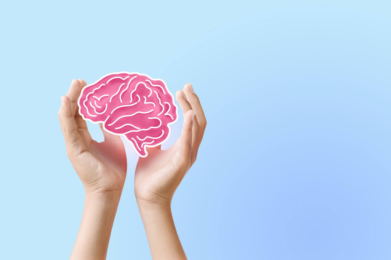 Mãos segurando ilustração de cérebro em fundo azul, representando cuidados com a saúde cerebral e hábitos para apoiar o bem-estar mental.