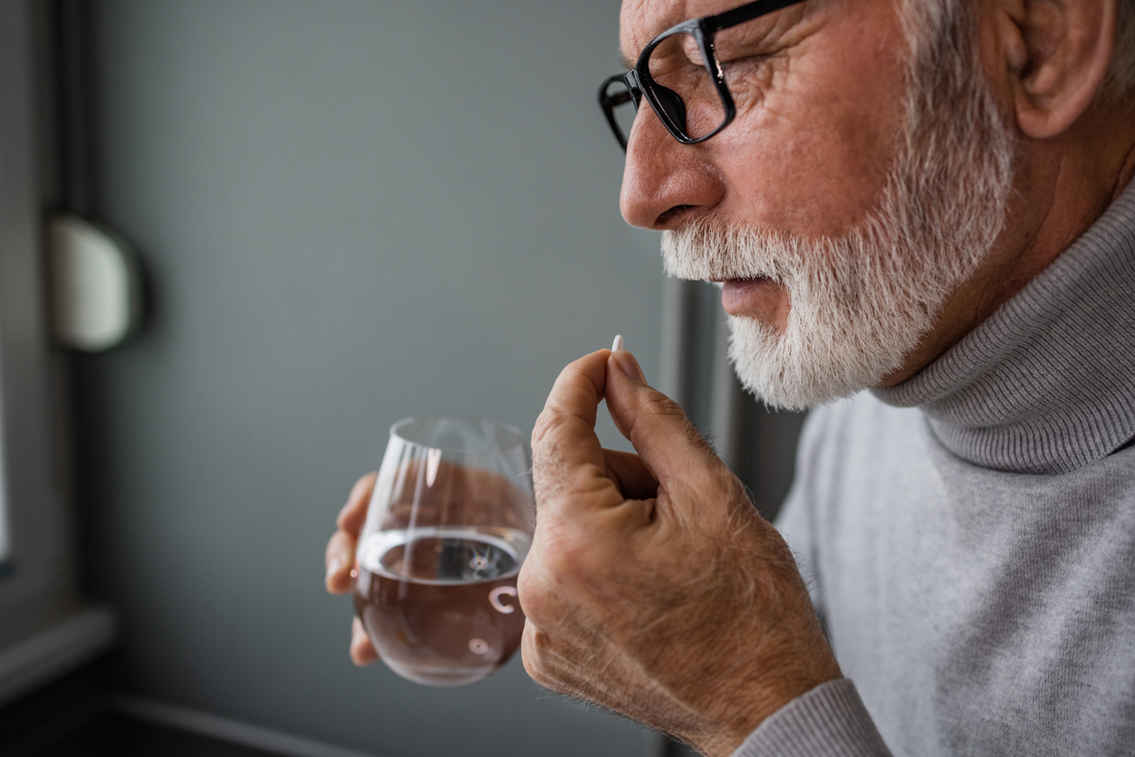 Homem idoso tomando cápsula com água, em imagem relacionada ao uso de suplemento alimentar para idoso no dia a dia.