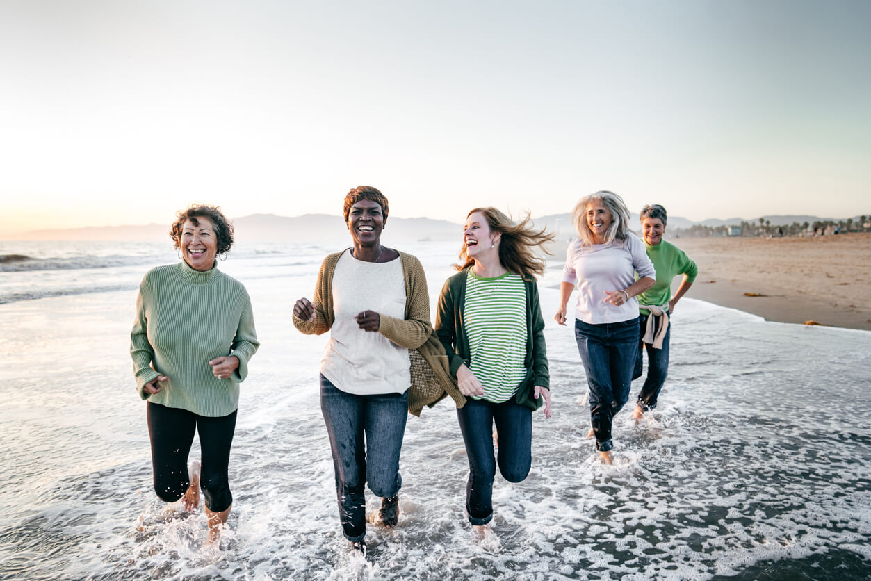 Mulheres maduras sorrindo e correndo à beira-mar, representando bem-estar e qualidade de vida da mulher na menopausa.