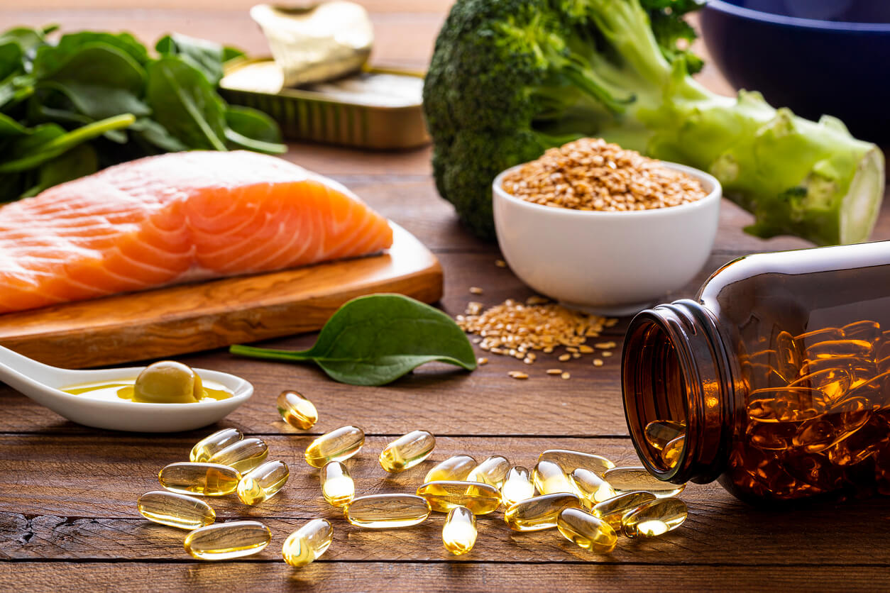 Salmão, espinafre, brócolis, sementes e cápsulas de vitaminas para memória sobre uma mesa de madeira.