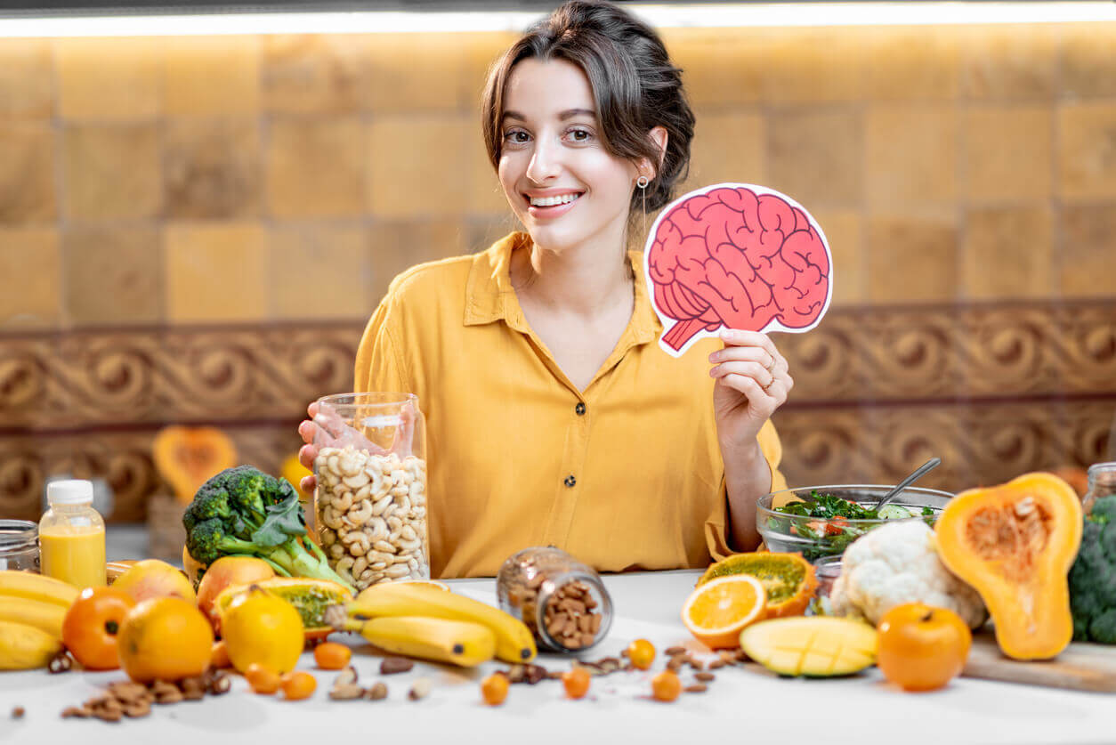 Mulher com alimentos saudáveis segurando ilustração de um cérebro, representando hábitos para manter o cérebro ativo.