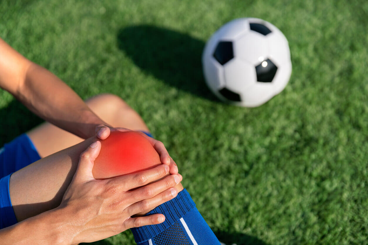 homem jogando futebol em um campo, com dor no joelho representando dor muscular.